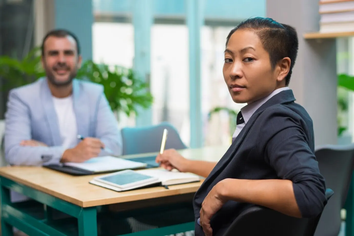 Уверенная брутальная женщина сидит за столом и смотрит в камеру.